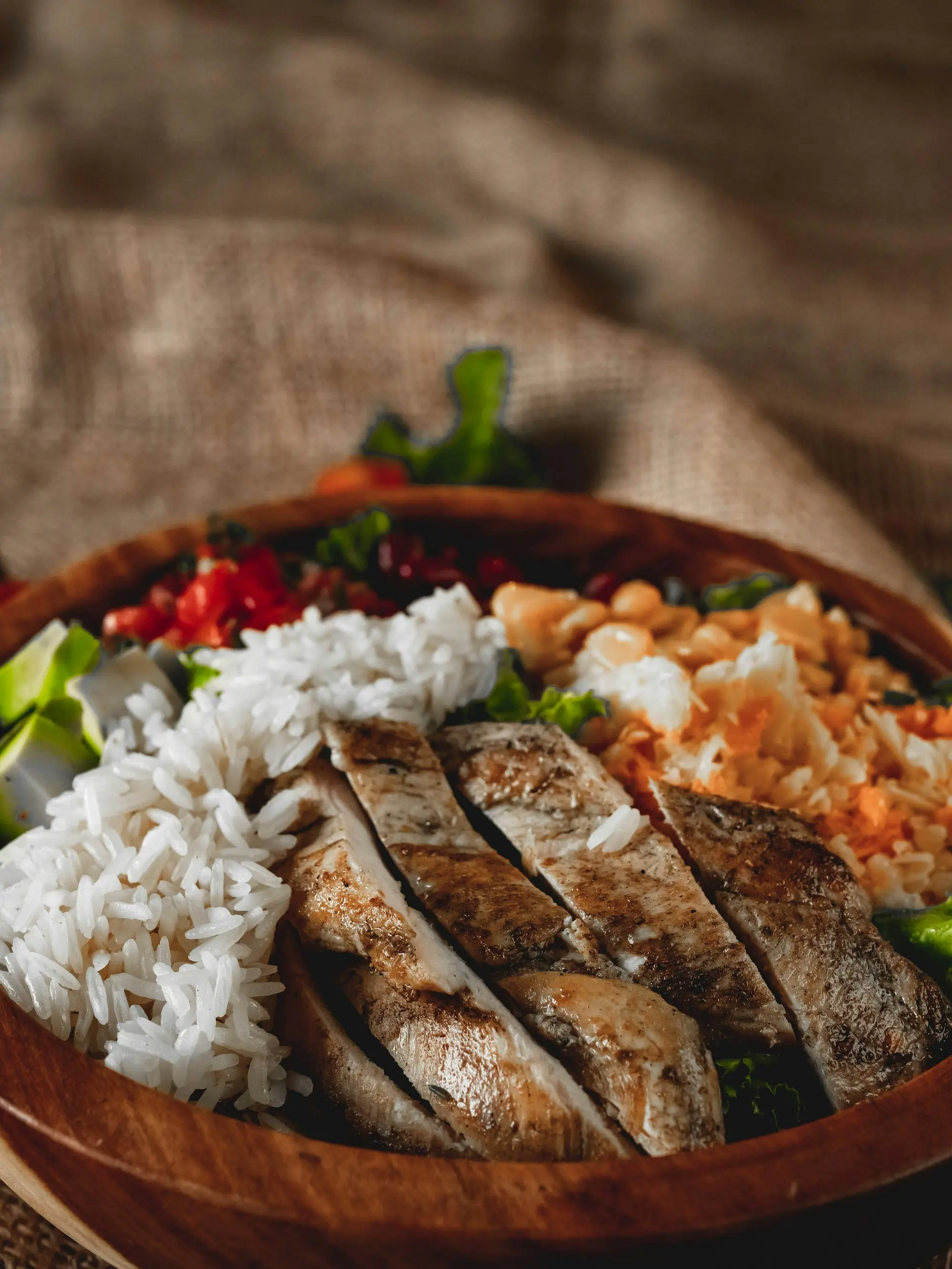 Sliced grilled chicken breast with white rice, chopped tomato salad and grilled peppers in a wooden bowl