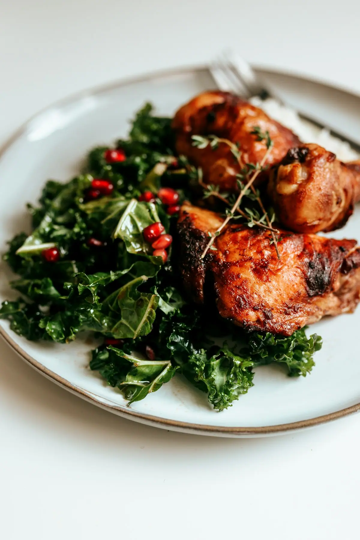 Roasted chicken thighs with a kale salad and a little rice on a white plate